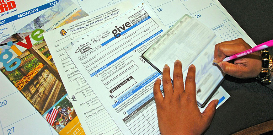 A Person hands writing a check for the Faculty and Staff Combined Giving Campaign