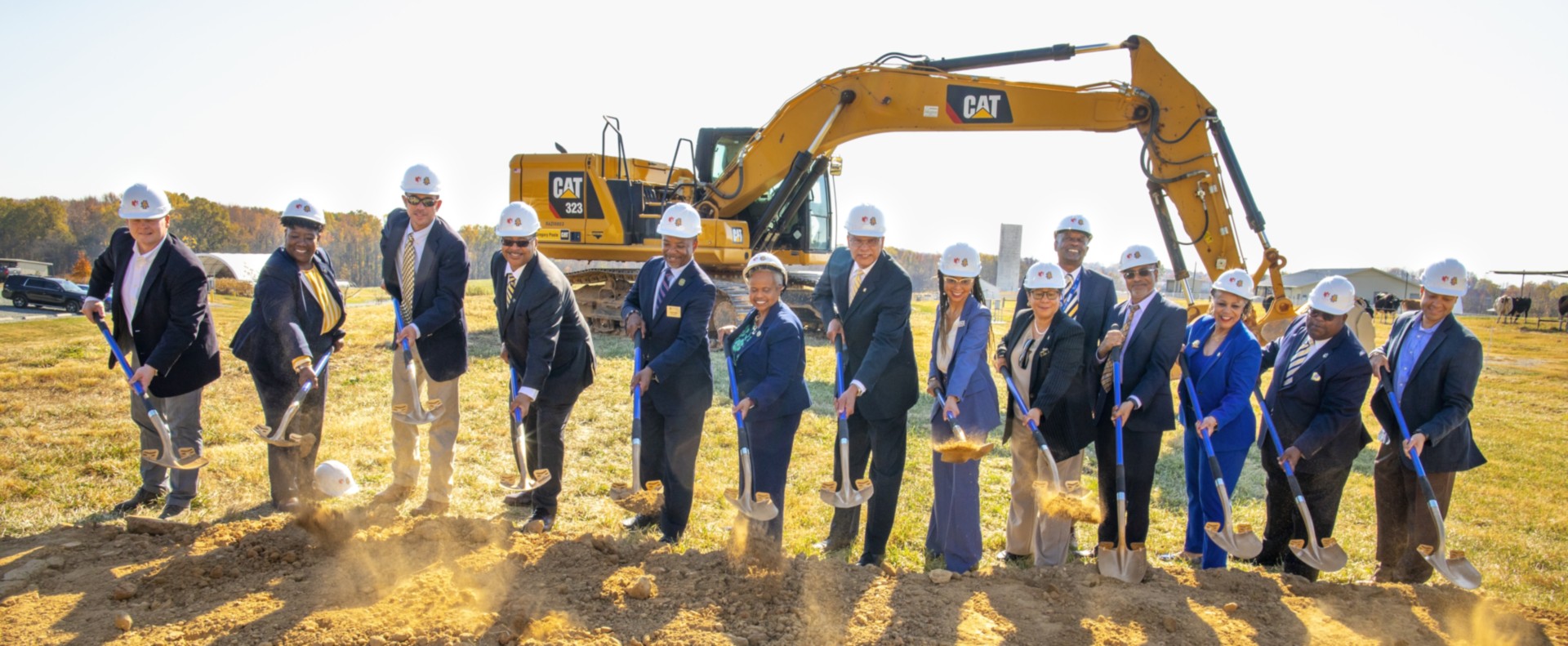 A group of people in suits and hard hats standing in front of a pile of dirt