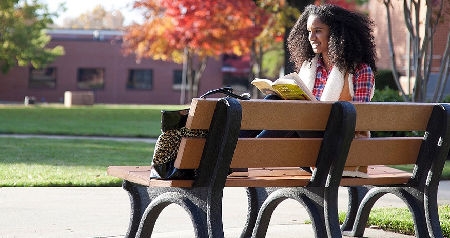 Student sitting outside reading near Aggie Village