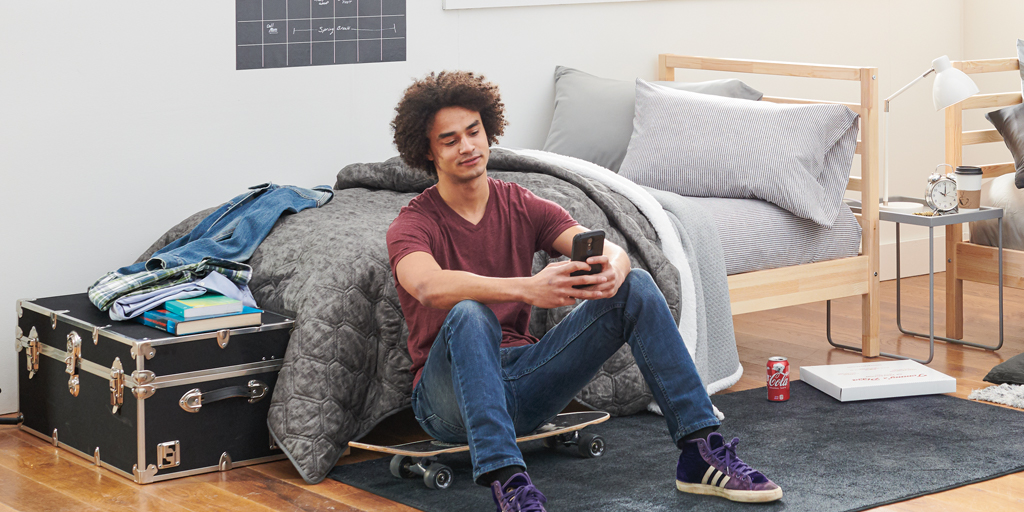 Young Man sitting on a skateboard looking at his phone in his dorm room.
