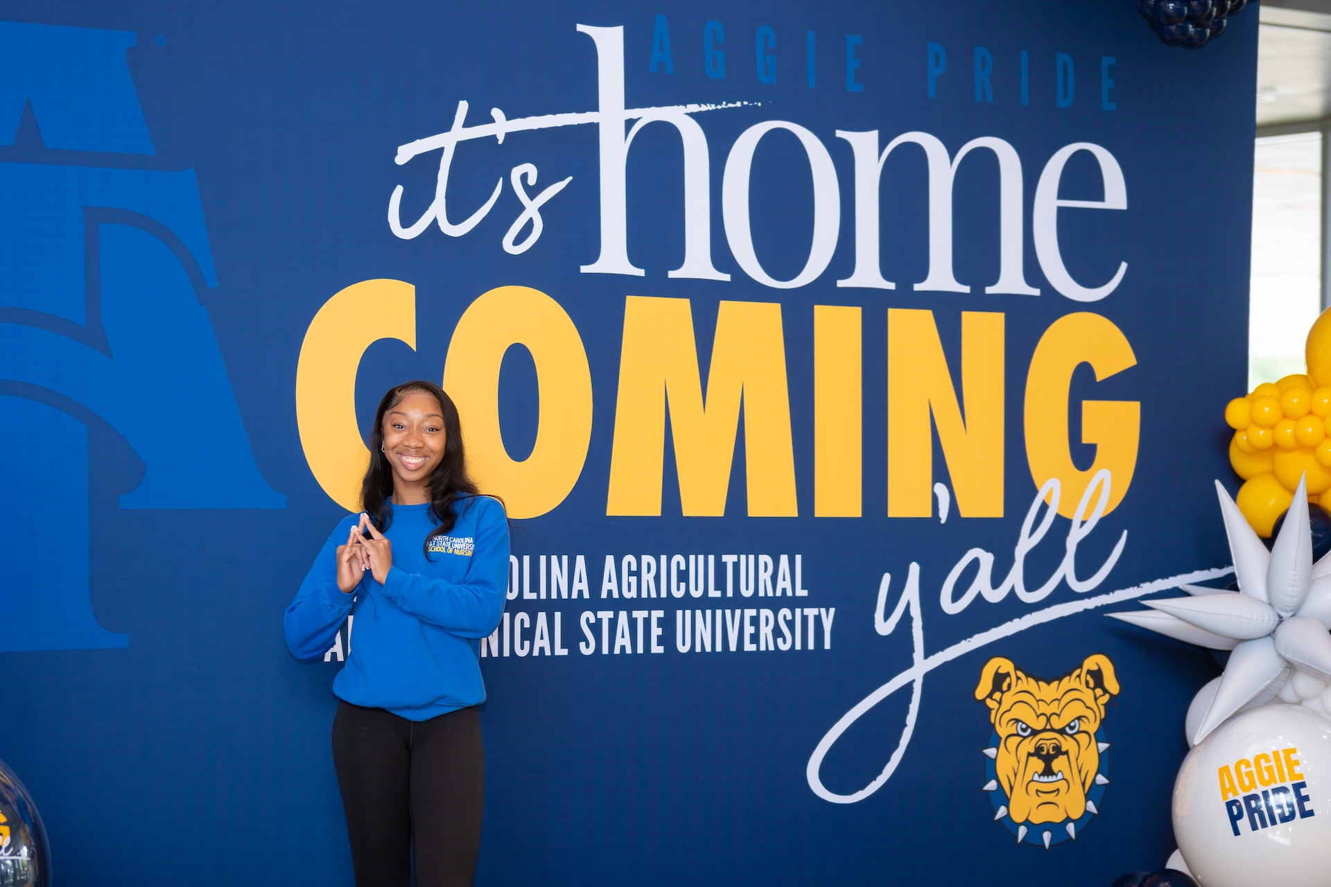 Miss Freshman smiling in front of the Student Center homecoming sign