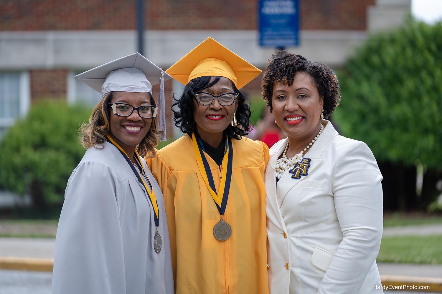 3 female Aggie alumni, 2 are wearing cap and gowns celebrating anniversary milestones