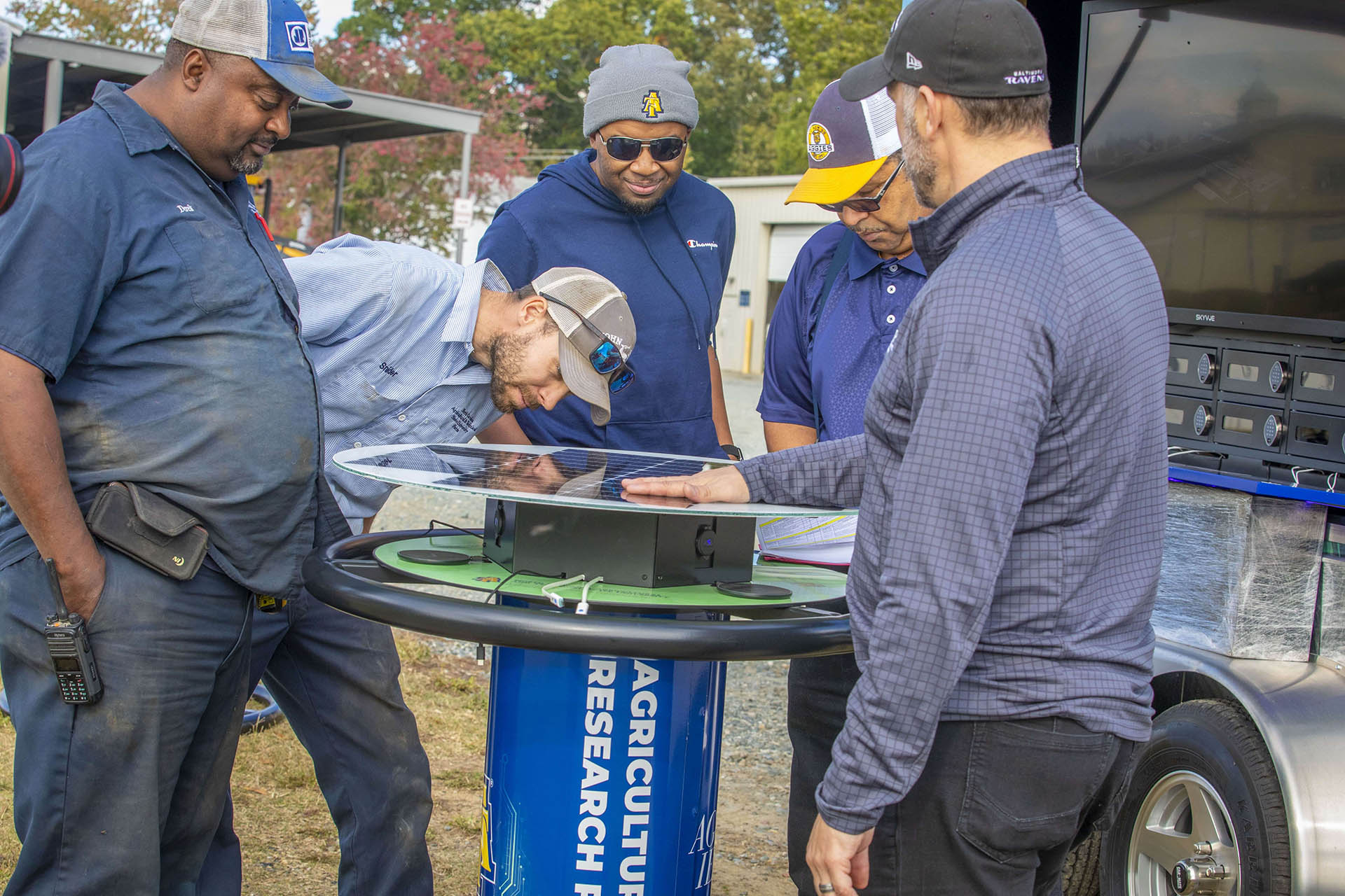 University Farm field staff inspect a table equipped with solar panels and charging cords, part of the solar-powered charging trailer the College of Agriculture and Environmental Sciences will use to present in the field.