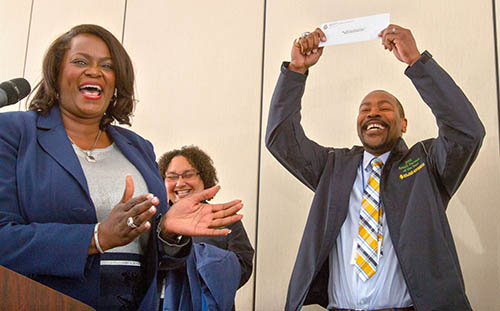 Dr. Rosalind Dale, left, claps behind a podium as Ronald Simmons accewpts his award as 2018 Small Farmer of the Year with an unidentified woman in the background