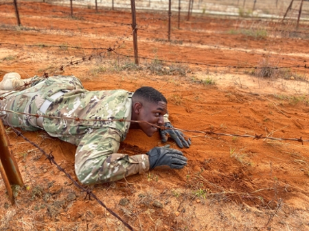 Army ROTC cadet crawling under bob-wire in the dirt